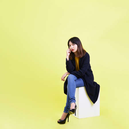 attractive young Asian woman sitting on the blank empty box on yellow background For job hunting ideasの写真素材