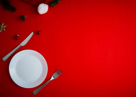 Minimal top view Christmas balls decoration and a white Empty plate with Set of fork, knife, and spoon  on a red backgroundの写真素材