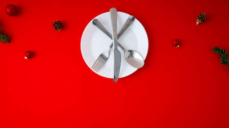 Minimal top view Christmas balls decoration and a white Empty plate with Set of fork, knife, and spoon  on a red backgroundの写真素材