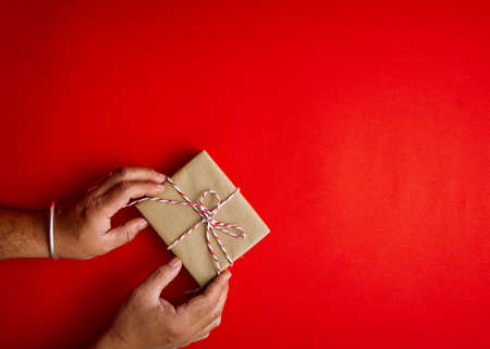 Male hands holding red gift box on a red background with copy space for your text