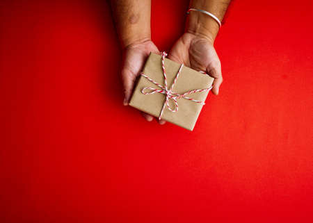 Male hands holding red gift box on a red background with copy space for your text