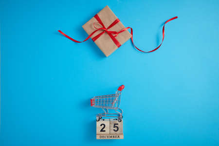Top view of a toy shopping cart with a gift box with wooden block Calendar on a blue background.