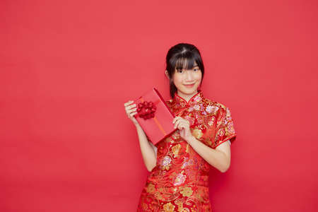 Portrait beautiful cute young Asian woman wear Chinese dress with red gift box for Chinese new year concept on a red backgroundの写真素材