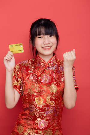 Portrait Cute young Asian woman wear Chinese dress with a credit card shopping online for Chinese new year on a red backgroundの写真素材