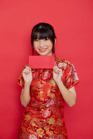 Cute Chinese woman holding a red envelope or Ang pow for New Year on a red background.の写真素材