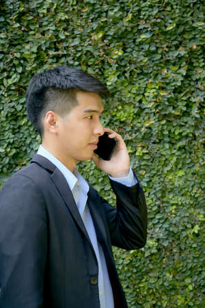 Young Asian businessman walking in the park using a smart phone.の写真素材