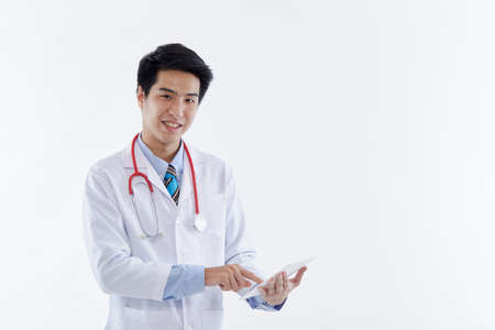 A friendly Asian male doctor in a white coat and red stethoscope using a tablet computer, modern medical technology on white background. medical technology conceptの写真素材