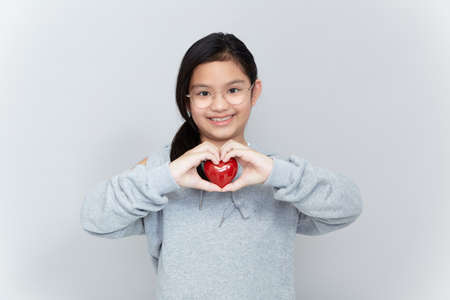 Portrait of a little girl holding a red heart Shape on gray backgroundの写真素材