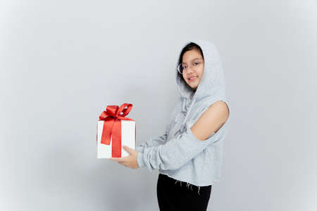 beautiful little girl with a gift and happy emotions on a gray background, a gift for the new year,...