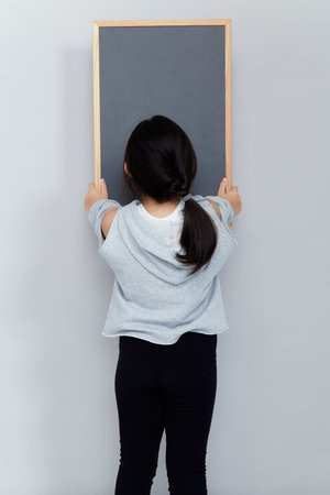 A young Asian girl turns back and holds a blackboard.