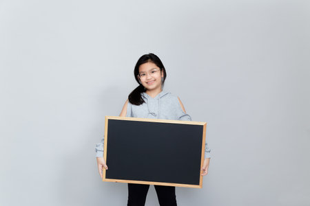 A little girl holds a blank chalkboard place for notification. Read this notification. Informing about the event. Cute schoolgirl with blackboard. Advertisement.の写真素材