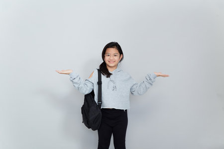 A cheerful smiling Asian Little girl wears a school bag isolated on a gray background.の写真素材