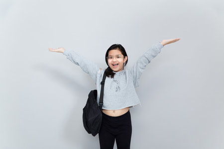 A cheerful smiling Asian Little girl wears a school bag isolated on a gray background.