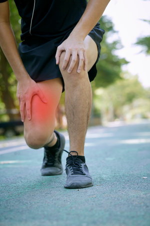 young sports man with strong athletic legs holding the knee with his hands in pain after suffering a...