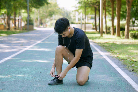 Young Asian Man Tying Shoelace Before Jogging In Summer Parkの写真素材