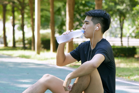 A young man sitting with a bottle of water rest after exercisesの写真素材