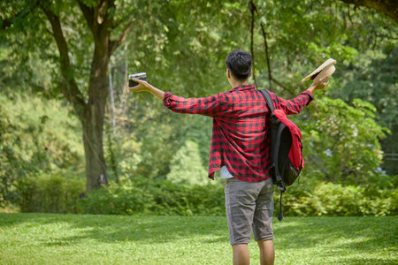 A young Asian backpacker holding a camera standing in a nature park.の写真素材
