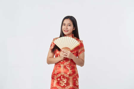 Attractive beautiful Young Asian woman in traditional red cheongsam dress holding Chinese fan for Chinese new year in light gray isolated studio backgroundの写真素材