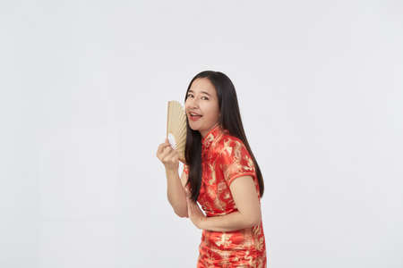 Attractive beautiful Young Asian woman in traditional red cheongsam dress holding Chinese fan for Chinese new year in light gray isolated studio backgroundの写真素材