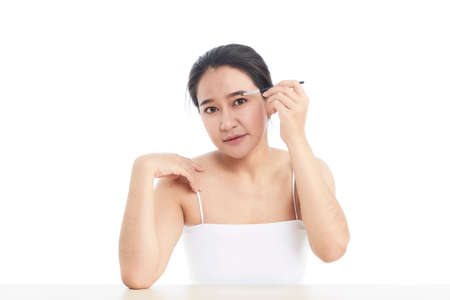 Beautiful Asian woman looking at the camera and with a small cosmetics brush in her raised a hand...