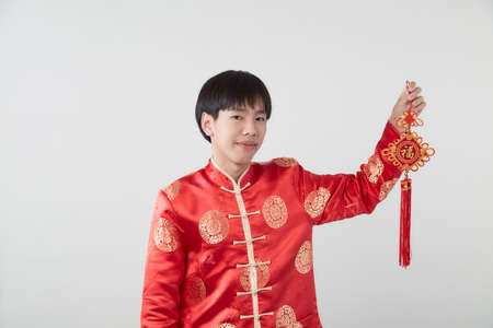 Portrait of Oriental young man with traditional clothing holding Chinese lucky word the Chinese word means congratulations and best wishes for a prosperous on light gray background for Chinese new year conceptsの写真素材