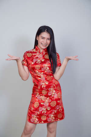 Happy Chinese new year. Beautiful Asian woman wearing traditional cheongsam qipao dress with gesture of congratulation isolated on light gray background with copy spaceの写真素材
