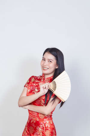Happy Chinese new year Asian woman wearing traditional cheongsam qipao dress holding fan isolated on light gray background with copy spaceの写真素材