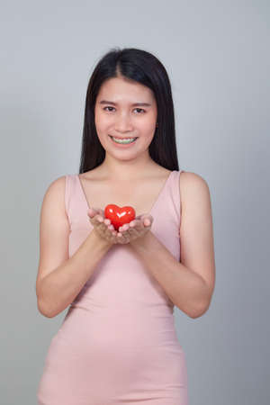 Portrait of beautiful Asian young woman holding pointing red heart shape isolated on light gray background with copy spaceの写真素材