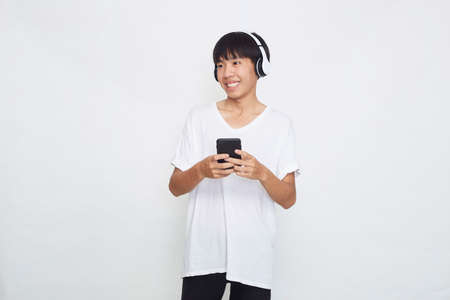 Young Asian man wearing headphones from a smartphone on white