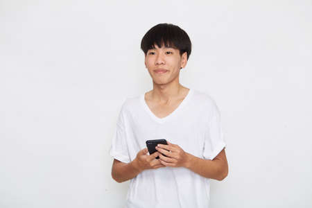 Handsome Young Asian man student texting messages using smartphone on a light background. Copy space and mockupの写真素材