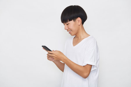 Handsome Young Asian man student texting messages using smartphone on a light background. Copy space and mockupの写真素材