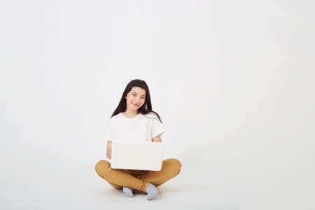 Back to school concept, Happy young Asian woman nice attractive sitting on the floor with crossed legs and using laptop on gray backgroundの写真素材