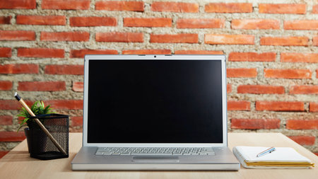 Laptop with blank screen on the desk and red brick wall work from home or study onlineの写真素材
