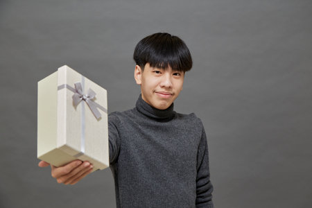 Holidays concept. young Asian man holding gift box studio shot, Isolated on gray backgroundの写真素材