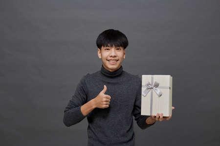 Holidays concept. young Asian man holding gift box studio shot, Isolated on gray backgroundの写真素材