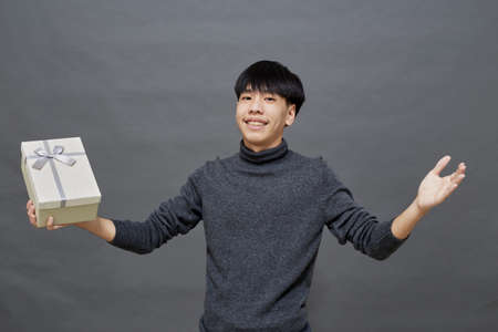 Holidays concept. young Asian man holding gift box studio shot, Isolated on gray backgroundの写真素材