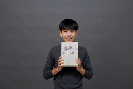 Christmas party and holidays concept. young Asian man holding gift box studio shot, Isolated on gray backgroundの写真素材