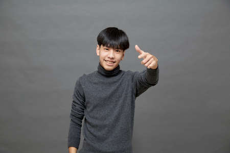 Portrait of Young Asian teenage cool hair stylish wearing grey sweater pointing finger studio shot...