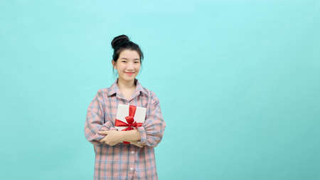 Portrait of a pretty smiling girl holding gift box and looking at camera isolated over blue background.の写真素材