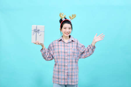 Portrait Cheerful cute woman holding gift box smiling wearing reindeer headband isolated blue color background. Christmas and new year sales joy conceptの写真素材