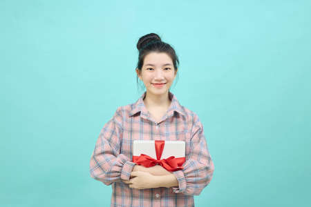 Portrait of a pretty smiling girl holding gift box and looking at camera isolated over blue background.の写真素材
