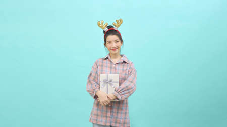Portrait Cheerful cute girl holding giftbox smiling wearing reindeer headband isolated blue color background. Christmas and new year sales joy conceptの写真素材