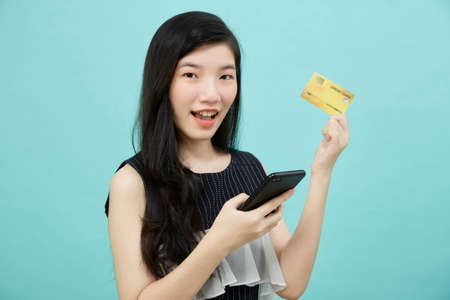 Beautiful Asian woman use smartphone and credit card payments online shopping online on light blue...