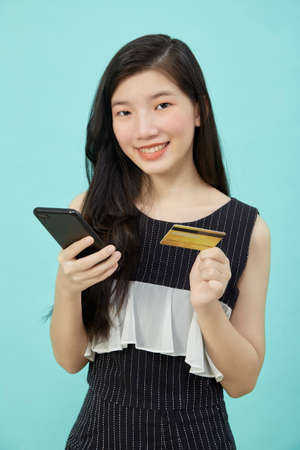 Beautiful Asian woman use smartphone and credit card payments online shopping online on light blue...