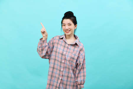 A young Asian woman pretty  pointing looking at ads wearing a plaid shirt standing and feeling happy and confident on blue backgroundの写真素材