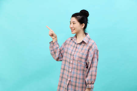 A young Asian woman pretty  pointing looking at ads wearing a plaid shirt standing and feeling happy and confident on blue backgroundの写真素材