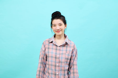 Cute asia girl smiling wearing a casual plaid shirt standing and feeling happiness and confident on blue backgroundの写真素材