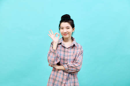 Portrait of a happy attractive young woman Asian posing in studio showing ok gesture on blue backgroundの写真素材