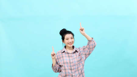 A young Asian woman pretty  pointing looking at ads wearing a plaid shirt standing and feeling happy and confident on blue backgroundの写真素材