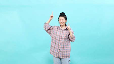 A young Asian woman pretty  pointing looking at ads wearing a plaid shirt standing and feeling happy and confident on blue backgroundの写真素材